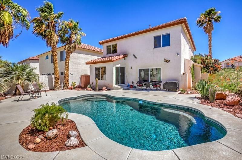 A cream-colored stucco home with red tile roofing and concrete backyard oasis featuring a dark teal pool and desert landscaping